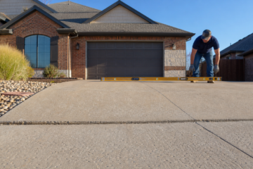 Contractor measuring a settled Amarillo concrete driveway with a long level
